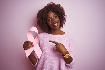 Young african afro woman holding cancer ribbon standing over isolated pink background very happy...