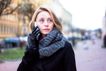 Sad pensive woman looks away, south day, talking on a cell phone. Lady on a cloudy day, a tired look on her face. Displeased young blonde holds a smartphone in his hand.