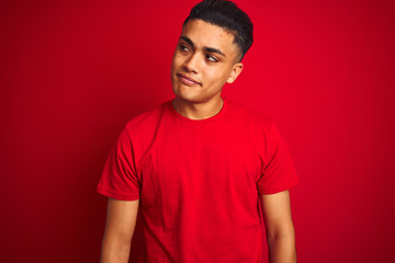 Young brazilian man wearing t-shirt standing over isolated red background smiling looking to the side and staring away thinking.