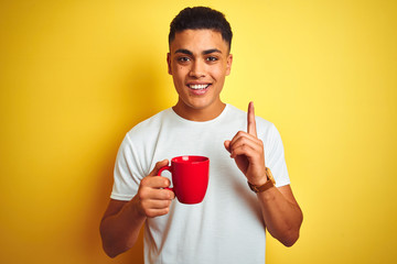 Young brazilian man drinking cup of coffee standing over isolated yellow background surprised with...