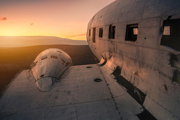 Damaged airplane on mountain against sunset.
