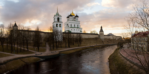 Fototapeta na wymiar Beautiful panorama of the medieval fortress with the bell tower and the Cathedral on the background of sunset. In the foreground flows the river Pskova. Pskov, Russia.