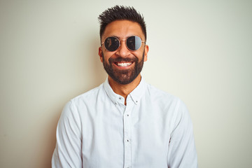 Handsome indian buinessman wearing shirt and sunglasses over isolated white background with a happy...