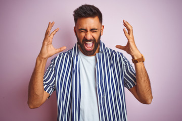 Young handsome indian man wearing summer striped shirt over isolated pink background celebrating mad and crazy for success with arms raised and closed eyes screaming excited. Winner concept