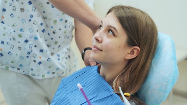 Dentist puts a dental bib on a girl sitting in a chair. Dental clinic.