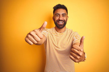 Young indian man wearing t-shirt standing over isolated yellow background approving doing positive...
