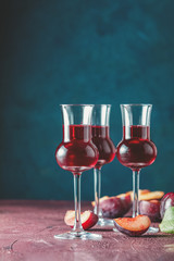 Plums strong alcoholic drink in grappas wineglass with dew. Hard liquor, slivovica, plum brandy or plum vodka with ripe plums on dark blue and  claret bordeaux concrete surface