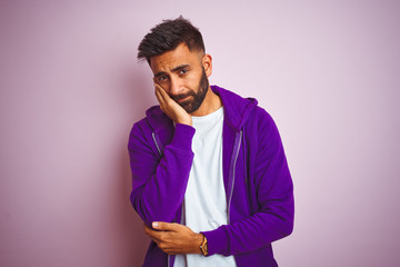 Young indian man wearing purple sweatshirt standing over isolated pink background thinking looking tired and bored with depression problems with crossed arms.