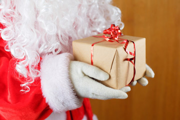 Santa Claus in white gloves and white beard holding gift box.