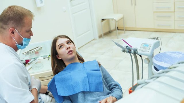 A young girl in the office at the dentist talks about teeth and problems. A male dentist is listening to a patient.