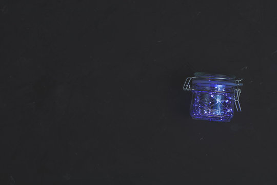 Christmas blue light in glass jar on black concrete surface background. Copy space, top view