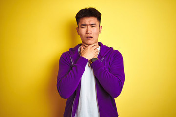 Fototapeta premium Young asian chinese man wearing purple sweatshirt standing over isolated yellow background shouting and suffocate because painful strangle. Health problem. Asphyxiate and suicide concept.