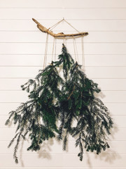 Stylish alternative christmas tree on white wall. Modern eco christmas tree made of pine branches, hanging on white rural wall in room. Happy Holidays. Festive decoration.