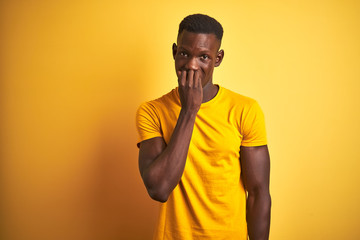 Young african american man wearing casual t-shirt standing over isolated yellow background looking stressed and nervous with hands on mouth biting nails. Anxiety problem.