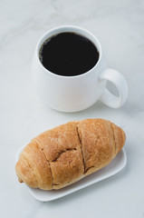 White mug with black coffee and croissant on white stone table. Coffee break.