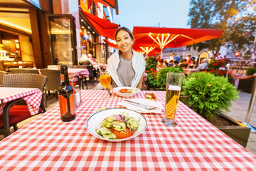 Happy Asian girl drinks a mug of lager beer in a traditional Bavarian restaurant and snacks on a...