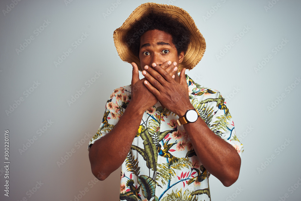 Poster Afro american man on vacation wearing summer shirt and hat over isolated white background shocked covering mouth with hands for mistake. Secret concept.