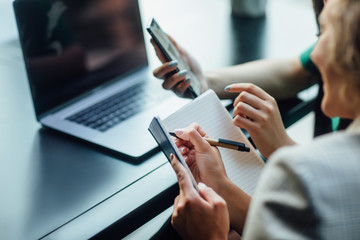 Close up photo, female business partners while reading a journal together in an outdoor cafeteria. Writting something.