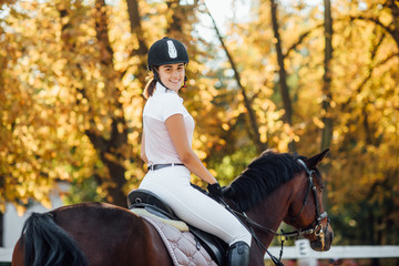 Photo of a beautiful young woman riding a horse in a black helmet and boots.