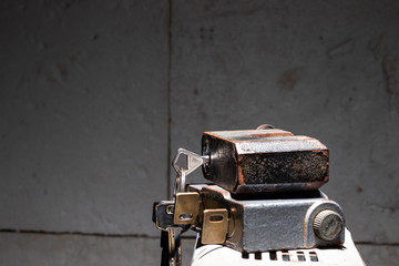 Two metal padlocks lying on top of each other with keys inserted in them against the background of the garage wall. Close-up side view.