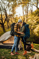 Young beautiful couple with hiking backpack kissing in the forest near tent. Attractive woman and handsome man relaxing together in nature. Instagram mood stories picture.