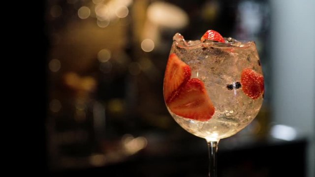 Gin and tonic strawberry with juniper rotating with bar background in red color. Gin tonic cup. Fixed plane.