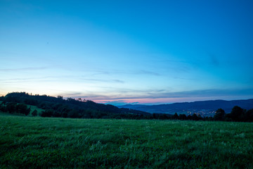 Fototapeta premium Multi colored sky of hill Velka Lhota Beskydy area sky and clouds play with many colors with view to surround the nature area around many small hills and mountains around capturing during sunset.