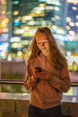 Teenager Mädchen mit Smartphone vor den Lichtern der Moskauer Skyline