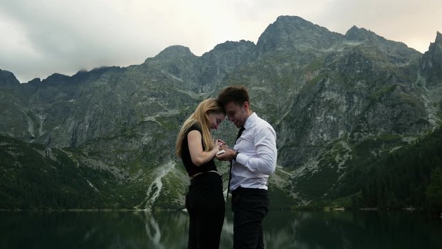 Man in costume makes a marriage proposal to his beloved woman near a evening mountain lake, puts on a engagement ring on happy surprised girl