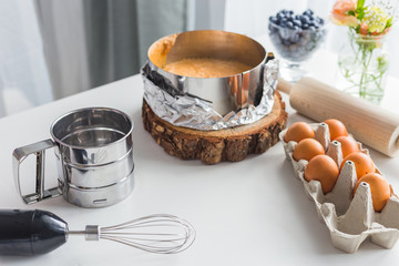 Homemade delicious sponge cake or soft cake with ingredients: eggs, berries, rolling pin, metal flour sifter on wood table with copy space. Bakery concept. Copy cpace