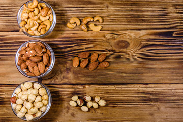 Various nuts (almond, cashew, hazelnut) in glass bowls on a wooden table. Vegetarian meal. Healthy eating concept. Top view