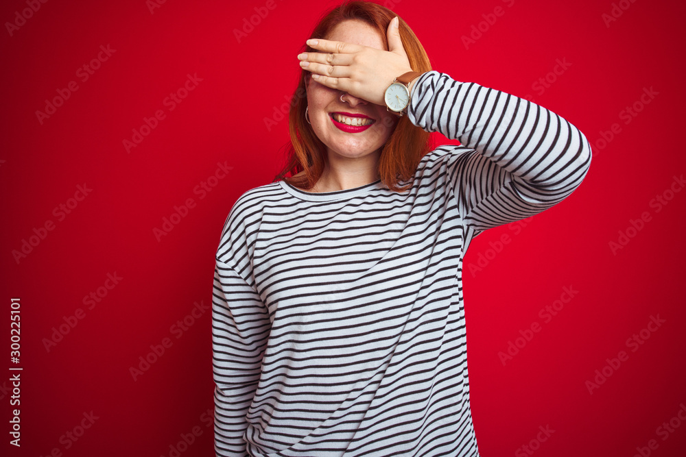 Canvas Prints Young redhead woman wearing strapes navy shirt standing over red isolated background smiling and laughing with hand on face covering eyes for surprise. Blind concept.