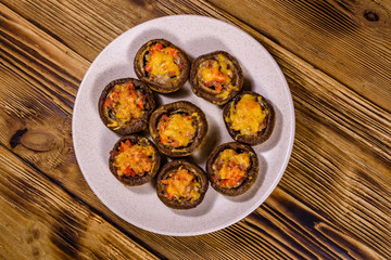 Baked champignons stuffed with minced meat and cheese in plate on a wooden table. Top view