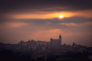 Obraz premium Beautiful Italian landscape with rolling hills, silhouette of old castle, vineyards and dramatic clouds at sunrise. Warm tones