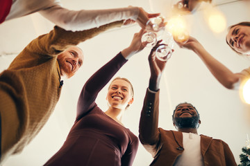 Low angle view at multi-ethnic group of people e clinking champagne glasses during Christmas party,...