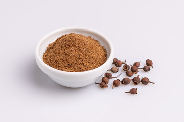 Ground allspice in white ceramic bowl isolated on white background, soft light, studio shot, copy space.  Also called Jamaica pimenta, or myrtle pepper. Latin name 