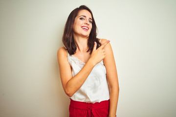 Young beautiful woman wearing t-shirt standing over white isolated background cheerful with a smile of face pointing with hand and finger up to the side with happy and natural expression on face