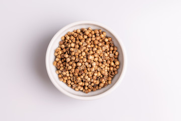 Coriander seeds in white ceramic bowl isolated on white background, soft light, studio shot, copy space