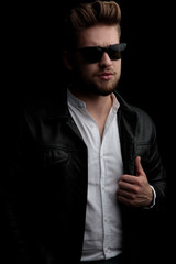 man wearing sunglasses standing and looking away while fixing jacket