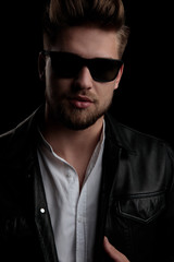 good looking casual man wearing sunglasses standing and adjusting  jacket
