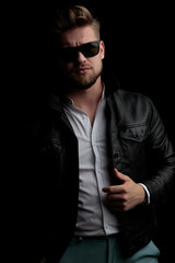Obraz premium casual man wearing sunglasses standing and fixing his leather jacket