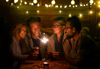 Happy family of four people sparkling wishing a wonderful new year 2020. Large pizza on the wooden table. Multi generation. Concept of happiness and love in a dark night