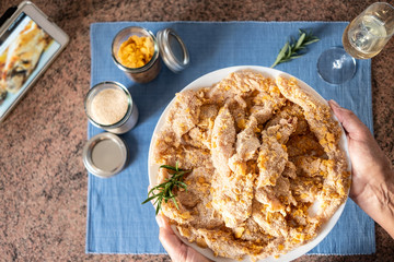 Above view of two female hands holding the dish with the chicken nuggets ready to be fried. Looking the recipe on the tablet next to her.