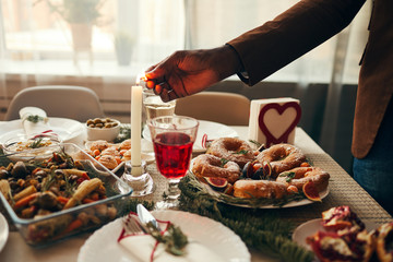 Closeup of hand lighting candle over rustic Christmas table with delicious homemade food decorated with fir branches, copy space