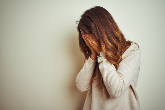Young beautiful woman wearing winter sweater standing over white isolated background with sad expression covering face with hands while crying. Depression concept.