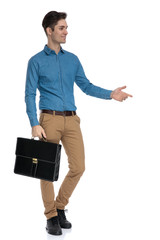 young elegant man holding suitcase and presenting to side