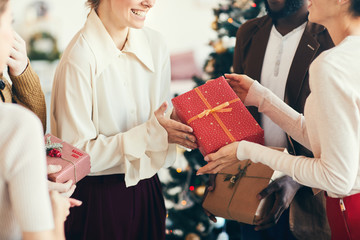 Cropped portrait of elegant young people exchanging gifts during Christmas party, focus on red box with golden ribbon, copy space