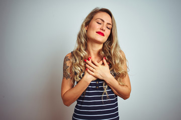 Young beautiful woman wearing stripes t-shirt standing over white isolated background smiling with hands on chest with closed eyes and grateful gesture on face. Health concept.