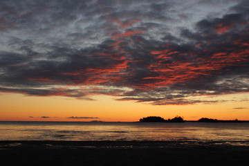 Fototapeta na wymiar Sunrise view from Vita Sannar, Dalsland. Multi colored clouds, small island and Lake Vanern.