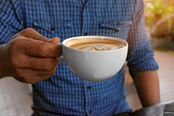 The young man holds a coffee cup to drink.